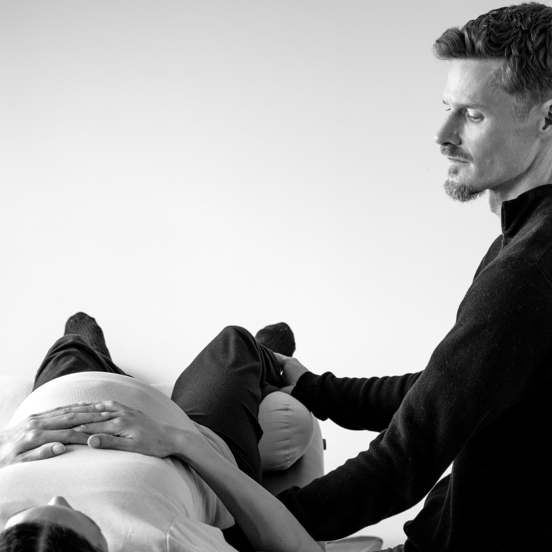 Craniosacral therapy session — therapist seated beside client on treatment table
